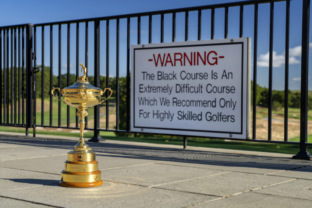 The Ryder Cup trophy in front of the Bethpage Black warning sign